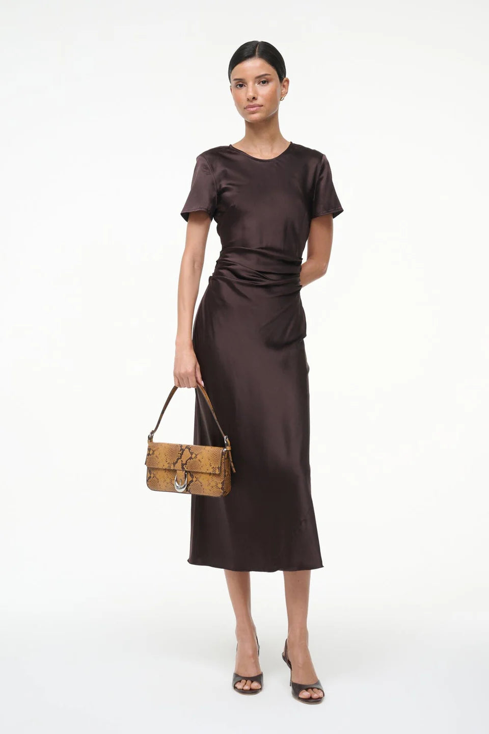 Woman wearing a brown dress holding a patterned handbag on a white background