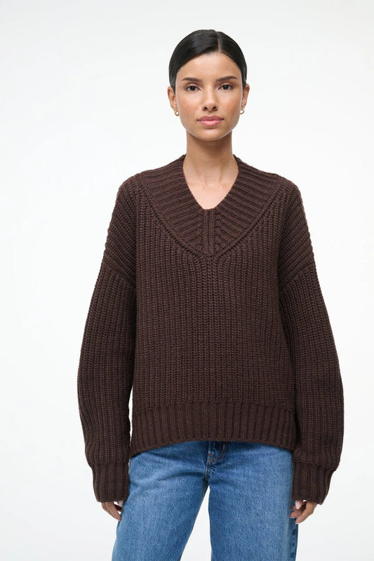 Woman wearing a brown sweater and blue jeans on a white background