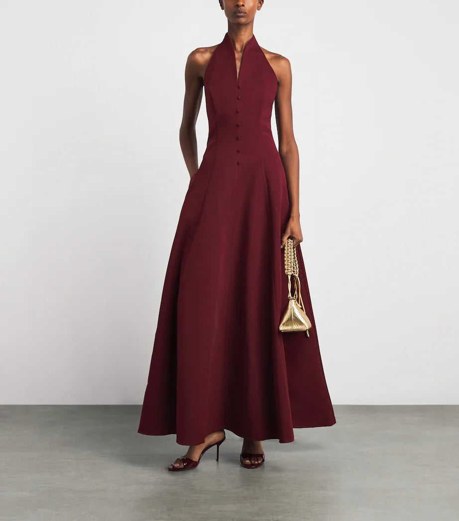 A model wearing the Staud Carmino Stella dress which features button detailing along the front holding a gold purse and wearing red heels.
