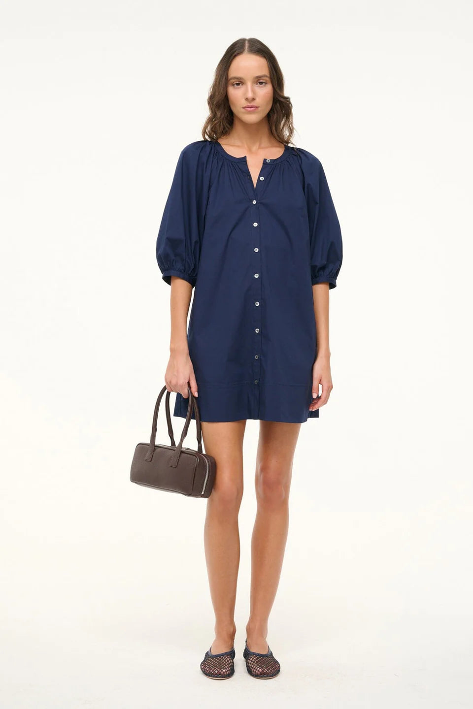 Woman wearing a navy blue dress holding a brown handbag on a white background