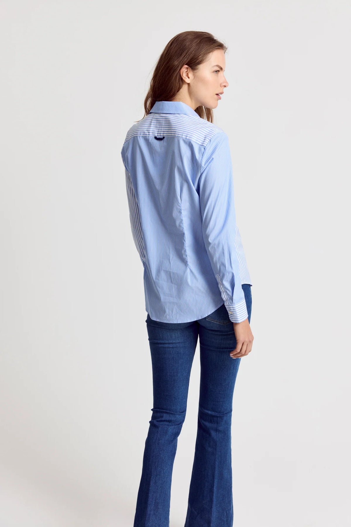 Woman wearing a light blue stripe long sleeve button up shirt and dark blue jeans on a white background