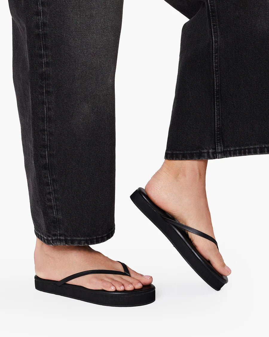Person wearing black platform Tkee flip-flops with black jeans on a white background