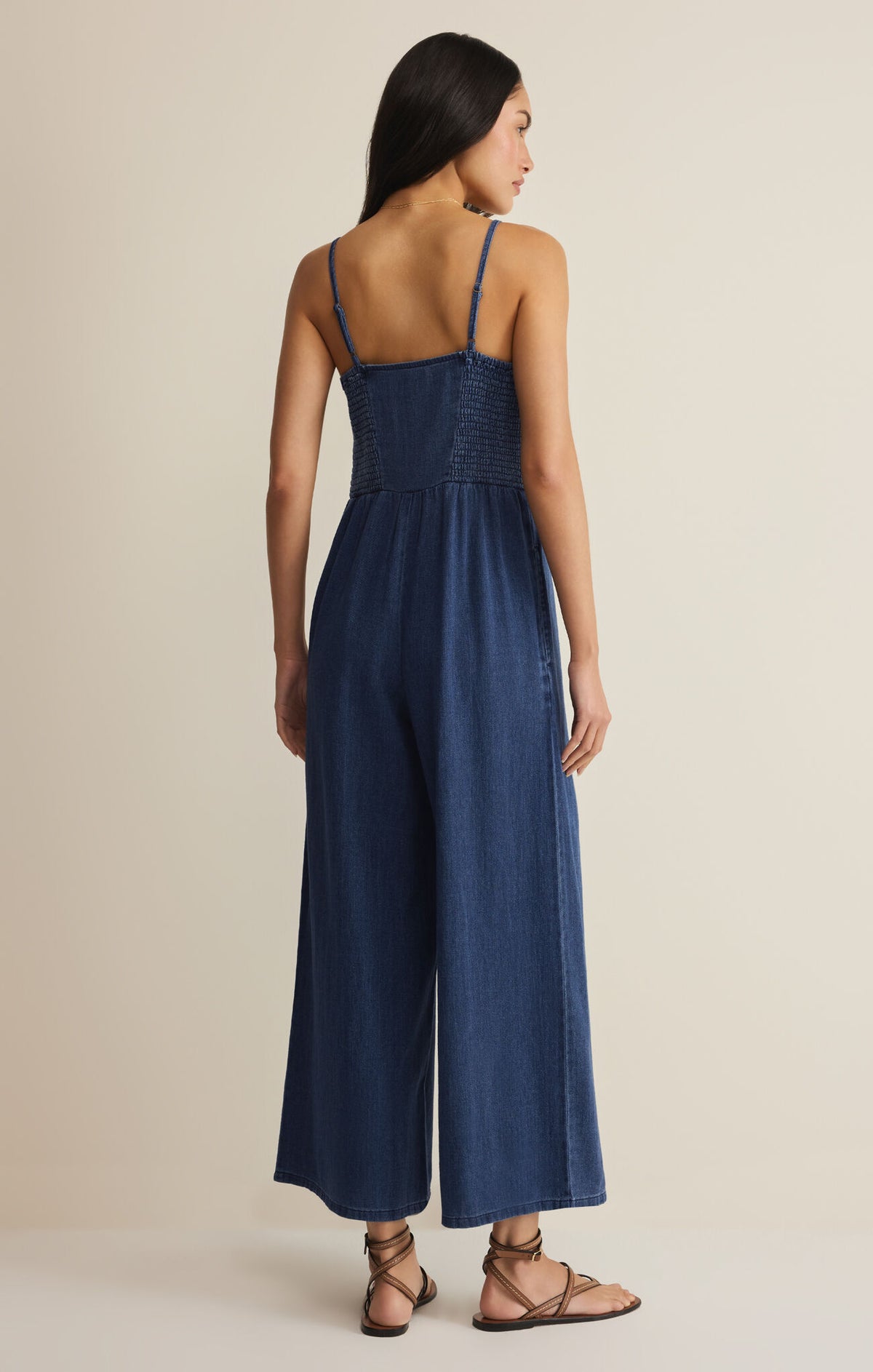 Woman wearing a blue sleeveless jumpsuit on a beige background