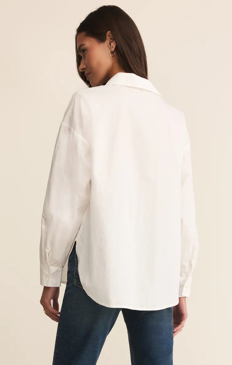 Person wearing a long sleeve button up white shirt and blue jeans on a beige background