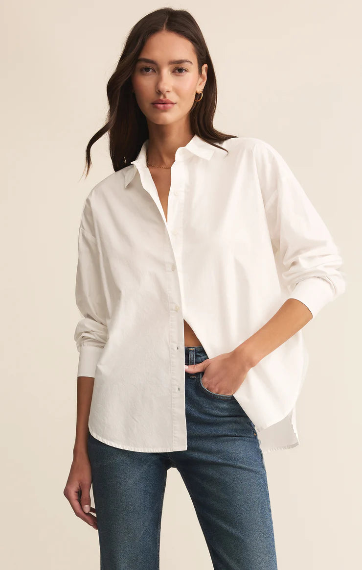 Woman wearing a white Long sleeve button up shirt and blue jeans against a beige background 