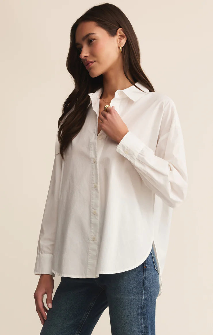 Woman wearing a white long sleeve button up shirt and blue jeans against a beige background