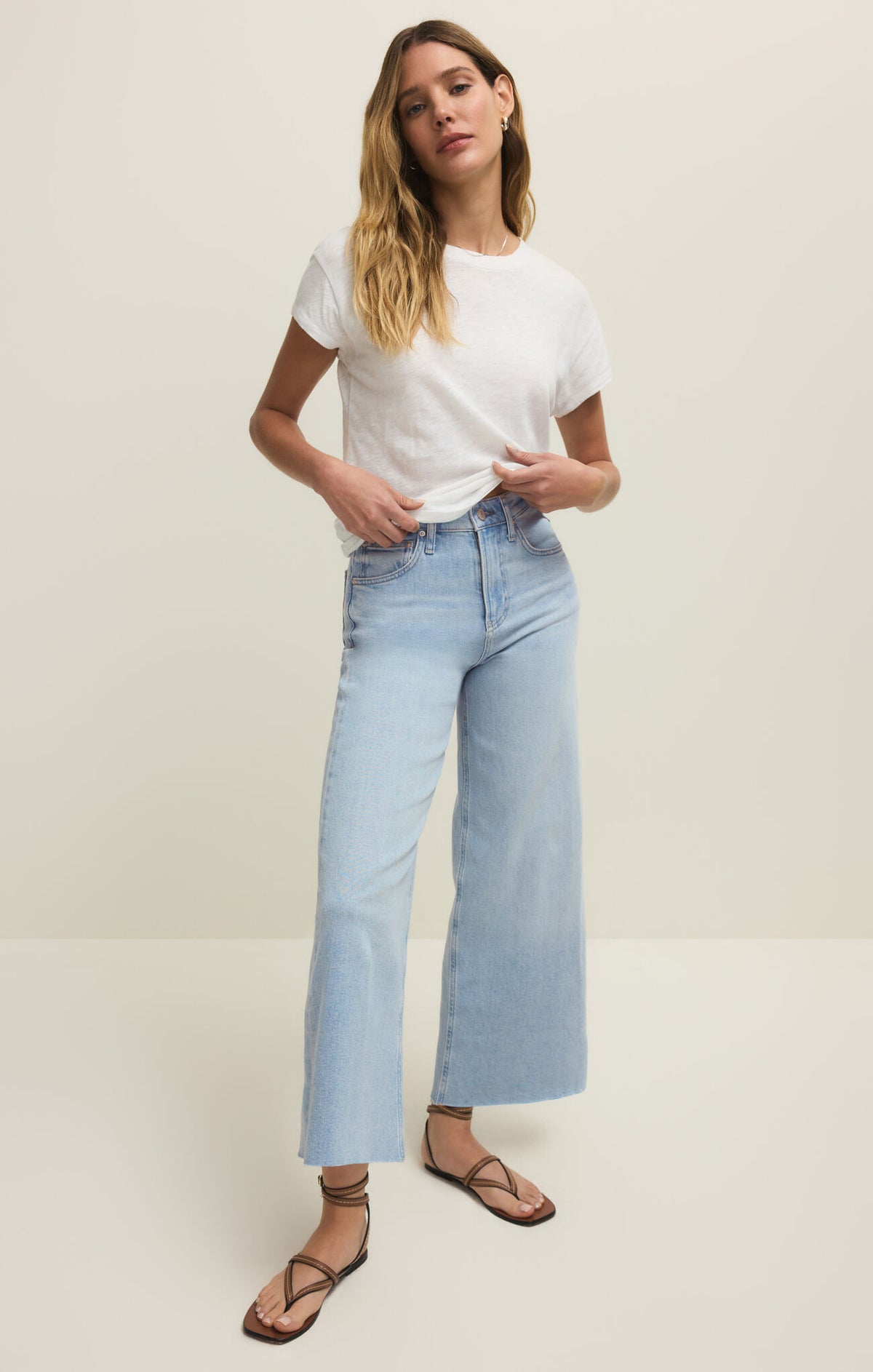 Woman wearing a white t-shirt and light blue cropped jeans on a plain background