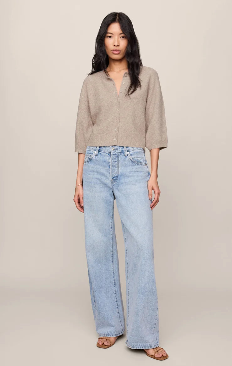 Woman wearing a beige cardigan and light blue jeans against a plain background