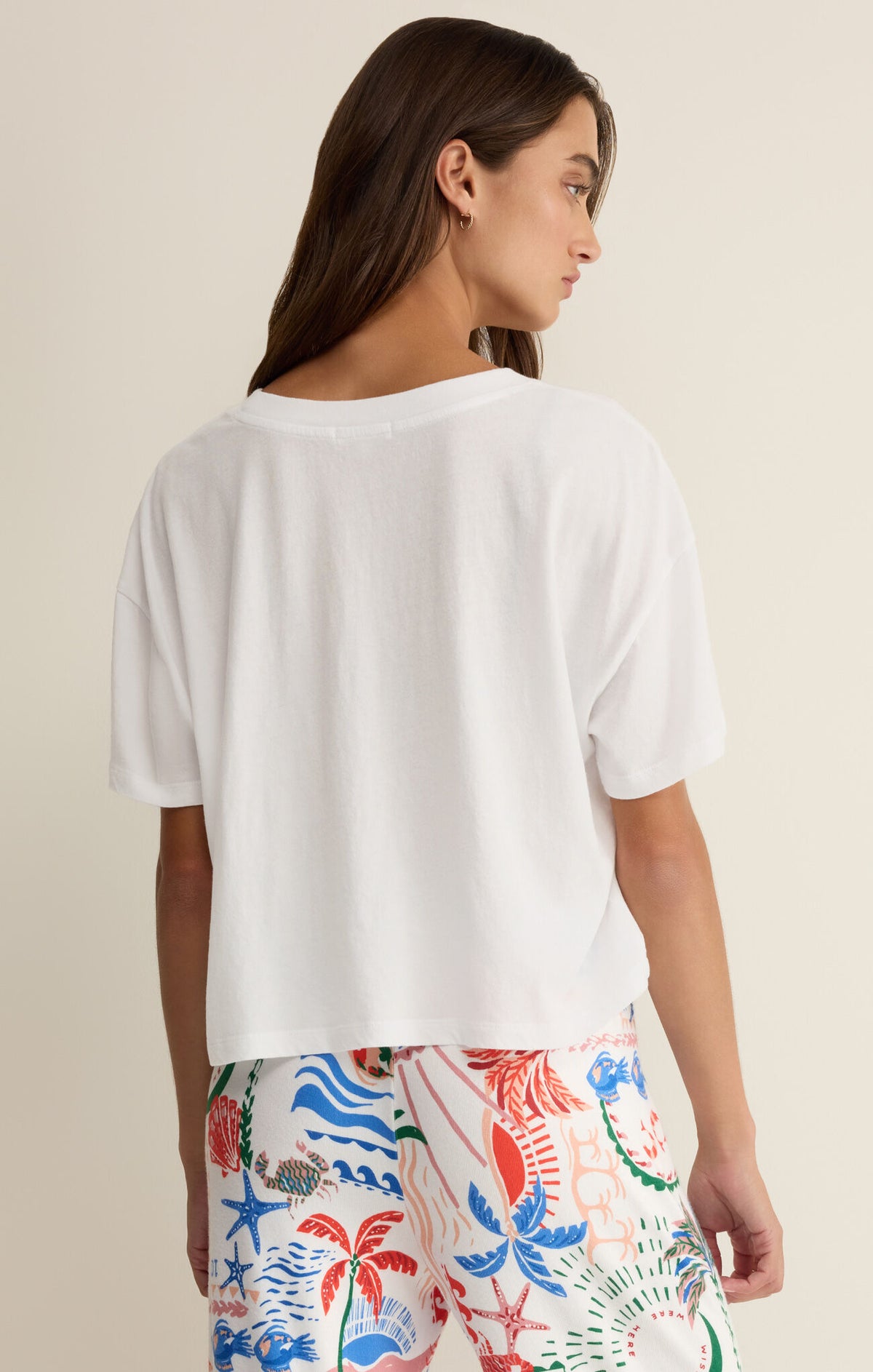Woman wearing a white t-shirt and colorful floral pants on a beige background