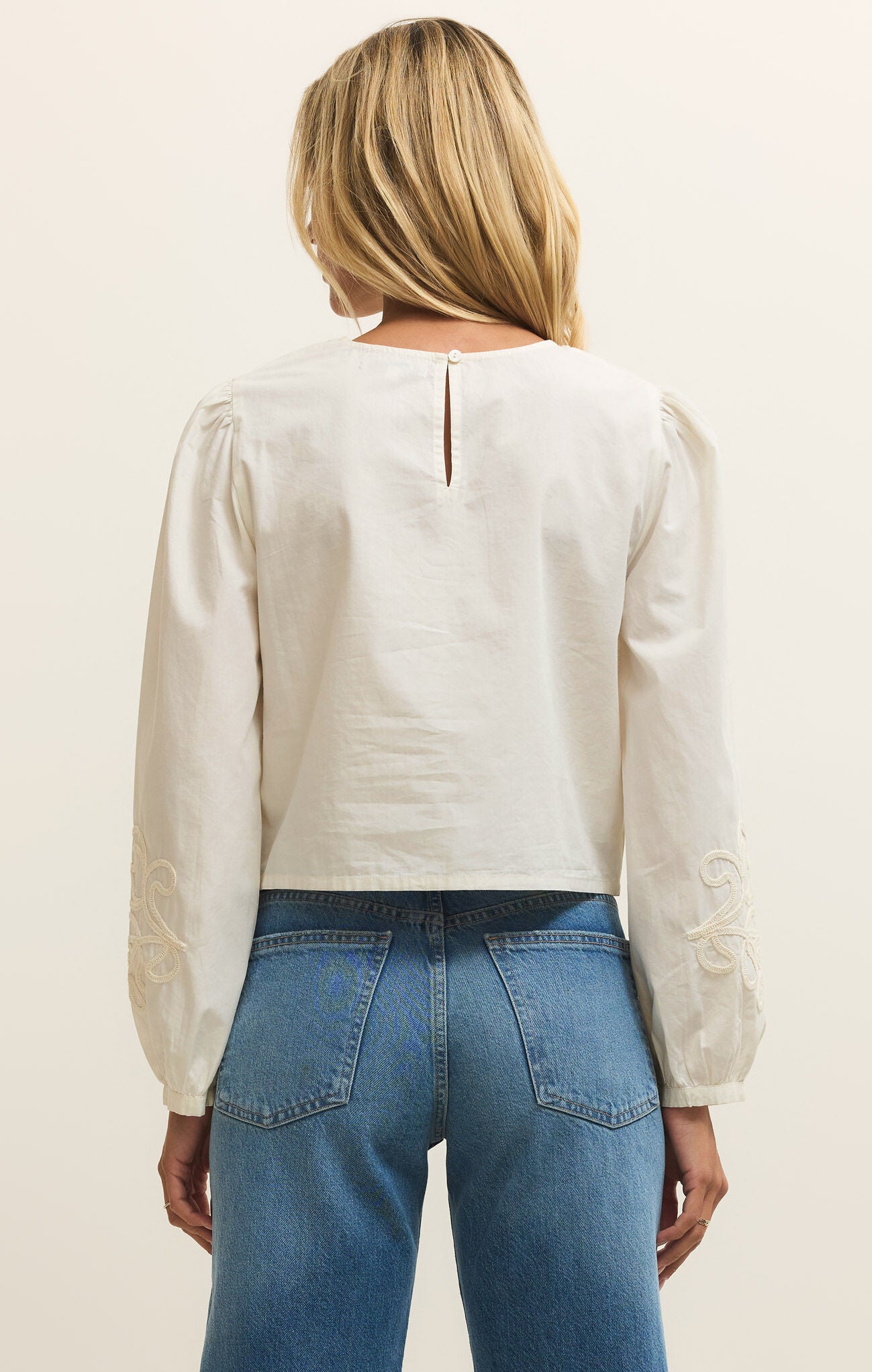Person wearing a white blouse and blue jeans on a plain background