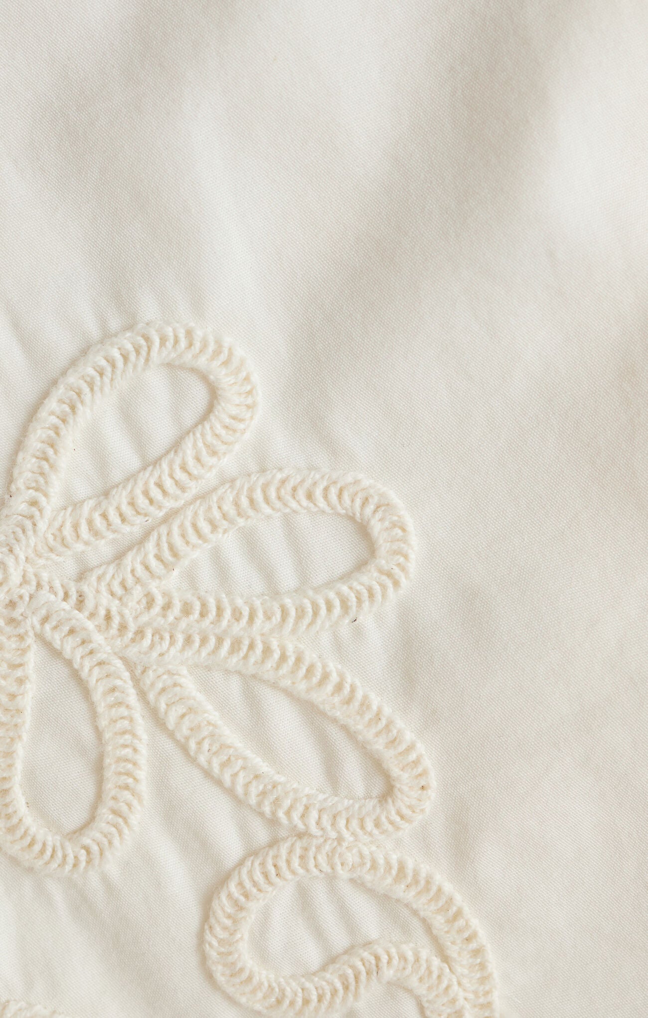 Close-up of a textured white fabric with a decorative pattern on a light background